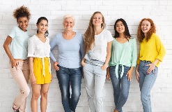 Photo of a group of diverse women smiling in front of a white brick wall.